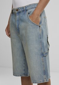 Lichtblauwe spijkershorts met een relaxed fit, voorzien van frontzakken, een cargozak aan de zijkant en zichtbare stikseldetails.