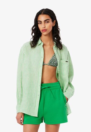 Camisa de botones a rayas verdes sobre un bikini verde, combinada con pantalones cortos verdes lisos. Presenta un corte relajado y una tela texturizada.