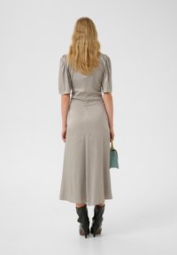 Light grey midi dress with a textured finish, short puff sleeves, and a fitted waist. Paired with black knee-high pointed-heel boots.