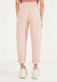 Ljusrosa, högmidjade denimbyxor med elastisk midja, avslappnad passform och uppvikta fållar. Bakfickor synliga. Bärs med vita sneakers.