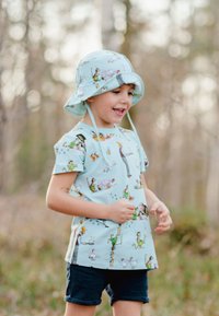 Ljusblå kortärmad skjorta med lekfulla djur- och karaktärstryck, tillsammans med en matchande bucket hat och mörka shorts.