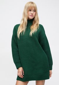 Zaļš adīts džemperkleita ar augstu apkakli, ribotām aprocēm un teksturētu rakstu. Dizains ir vaļējs, pāraizmēra piegriezums.