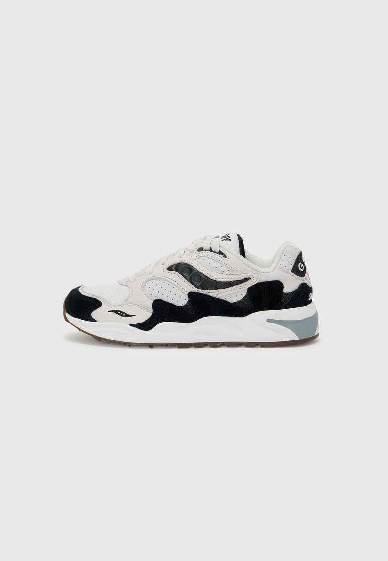 Zapatilla deportiva blanca y negra con paneles de ante y malla, cordones blancos y suela gruesa blanca con acentos en gris y goma.