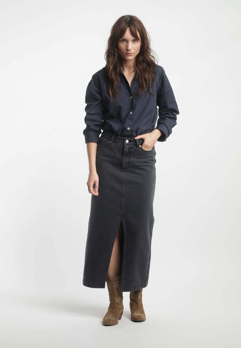 Chemise bleu marine à boutons, à manches longues, associée à une jupe maxi en denim noir avec une fente à l'avant, portée avec des bottes de cow-boy marron.