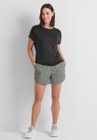 Black short-sleeve T-shirt made of smooth fabric, paired with light green shorts featuring front pockets and a relaxed fit. White sneakers.
