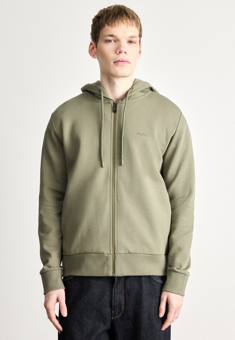 Felpa con cappuccio verde oliva con cerniera, realizzata in tessuto liscio, con cappuccio con cordino, polsini a costine e logo ricamato sul petto.