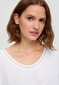 Weißes T-Shirt mit Rundhalsausschnitt, verziert mit einem dekorativen Saum am Kragen, aus leichtem, weichem Material.