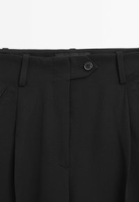 Svarta dressade byxor med midjeband, sidofickor, en knäppningsflik och en dold dragkedja framtill.