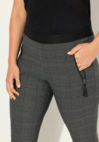 Svart- och grårutiga byxor med en bred elastisk midja och sidoficka med dragkedja som har en tofsdetalj. Tillverkade av bomullsblandning.