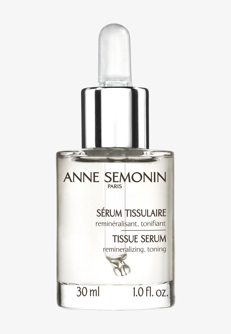 Botella de vidrio transparente para sérum con tapa de gotero plateada, etiquetada "Sérum Tissulaire" en texto marrón, tamaño de 30 ml. Diseño simple y elegante.