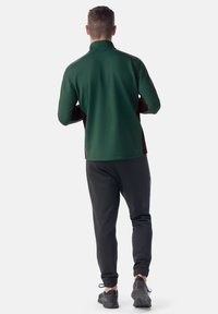 Top de manga larga verde oscuro con un cuello alto, combinado con pantalones jogger negros y zapatillas negras. Tela suave con diseño ajustado.