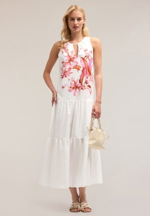 Robe blanche avec un design floral en rose et orange, sans manches, avec un encolure en trou de serrure, jupes tierées, accompagnée d'un sac léger et de sandales.