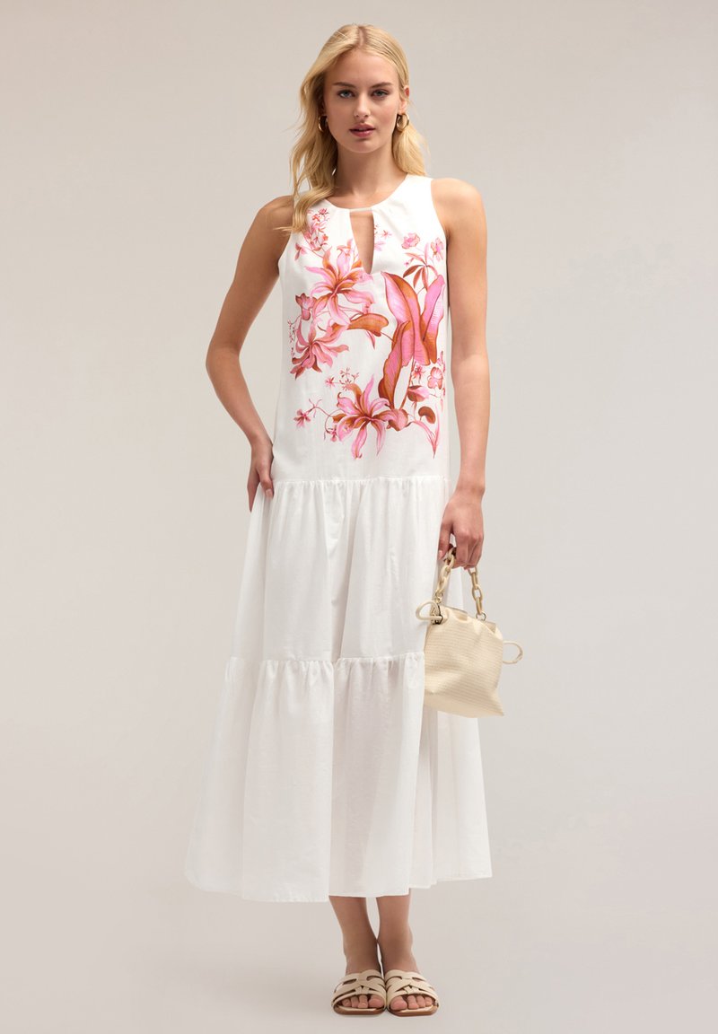 Rochie albă cu un design floral în nuanțe de roz și portocaliu, fără mâneci, cu decolteu tip găură cheie, fustă în straturi, asociată cu o geantă ușoară și sandale.
