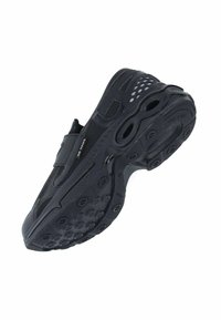 Chaussure de sport noire avec tige en mesh et semelle en caoutchouc, présentant des motifs de traction circulaires et des découpes sur les côtés pour la ventilation.
