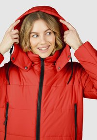 Veste matelassée rouge avec un col montant et une capuche amovible. Comprend une fermeture éclair sur le devant, des poches latérales et des accents noirs. Tissu lisse et brillant.