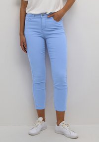 Jeans de tiro alto en un azul claro, con un corte ajustado, que cuentan con bolsillos frontales y un cierre con un solo botón, combinados con zapatillas blancas.