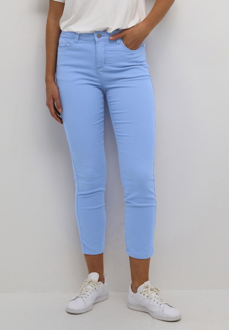 Jeans de tiro alto en un azul claro, con un corte ajustado, que cuentan con bolsillos frontales y un cierre con un solo botón, combinados con zapatillas blancas.