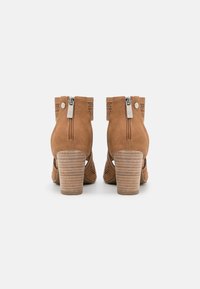 Botas de ante color cuero con acentos perforados, cremalleras laterales y tacones apilados con textura acanalada.