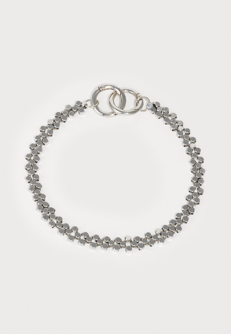 Srebrna bransoletka z połączonym wzorem, ozdobiona okrągłymi metalowymi koralikami i okrągłymi akcentami z metalowych elementów. Gładka tekstura z polerowanym wykończeniem.