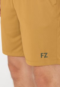 Gula sportshorts i slätt tyg, med en "FZ"-logga i mörkgrön på nedre vänstra sidan.