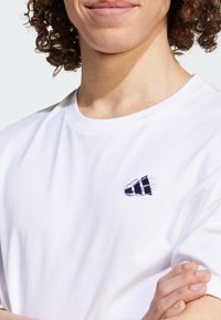 T-shirt bianca in cotone con logo ricamato nero e design in movimento sull'area sinistra del petto. Maniche corte, scollo a girocollo.