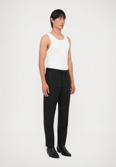 Calças pretas ajustadas com uma textura suave, combinadas com uma blusa sem mangas branca. O modelo está a usar sapatos de couro pretos. Design simples e minimalista.