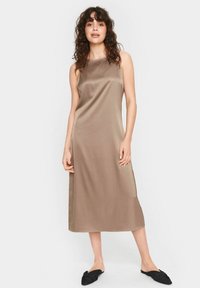 Satin midi kleita bēšā krāsā, bez piedurknēm ar taisnu fasonu. Iezīmējas ar gludu tekstūru un minimālistisku stilu, apvienota ar melniem apaviem.