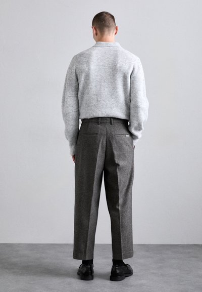 Grå strikket sweater med ribbet tekstur, parret med grå uldbukser i høj talje med en løs pasform og subtile sidelommer. Sorte sko.