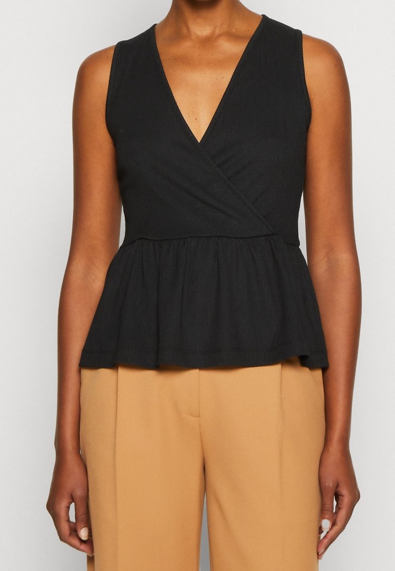 Haut noir sans manches avec un décolleté en V profond et un design portefeuille. Caractérisé par un ourlet à basque et un tissu texturé. Associé à un pantalon beige.