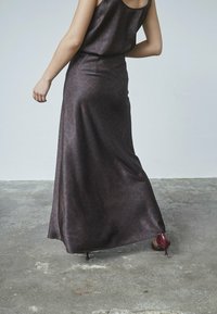 Maxi kjole i mørkebrunt satin med et subtilt dyrepatterne, ærmeløs design, flydende silhuet og sidedel, parret med bordeaux højhælede sko.
