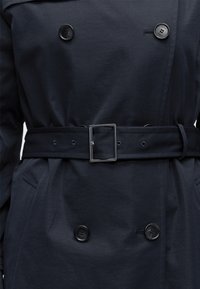 Σκούρο ναυτικό παλτό καμπαρντίνα με μαύρα κουμπιά και ασορτί ζώνη με τετράγωνη μεταλλική αγκράφα.