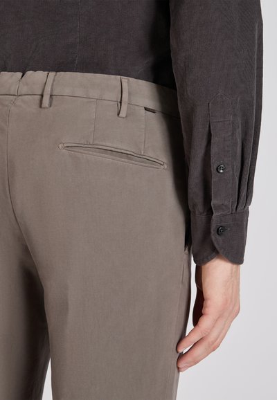 Szara koszula z kordy napami z zapięciem na guziki, w połączeniu z beżowymi spodniami z tylną kieszenią i gładką teksturą. Widoczne detale przeszyć.