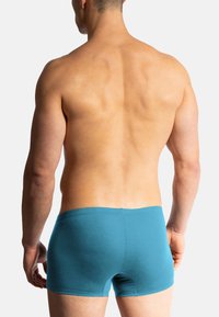 Tealfärgade bomullsboxershorts med en åtsittande passform, med sömlös midja och slät yta, visade bakifrån på en manlig modell.