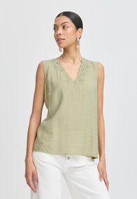 Top senza maniche di colore verde chiaro con scollatura a V e ricami floreali. Indossato con pantaloni bianchi, ha una vestibilità morbida e una texture delicata.