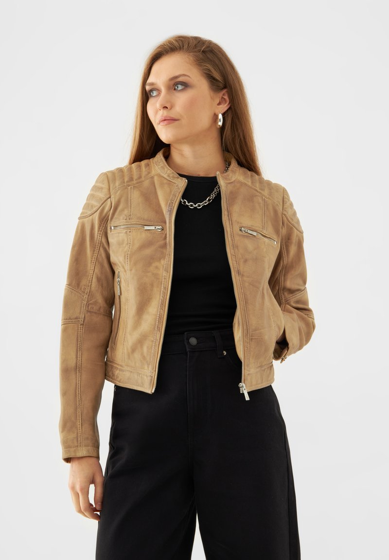 Brun läderjacka med hög krage, blixtlåsfickor, ribbade axelaccenter och en figursydd design, bärs över en svart topp.