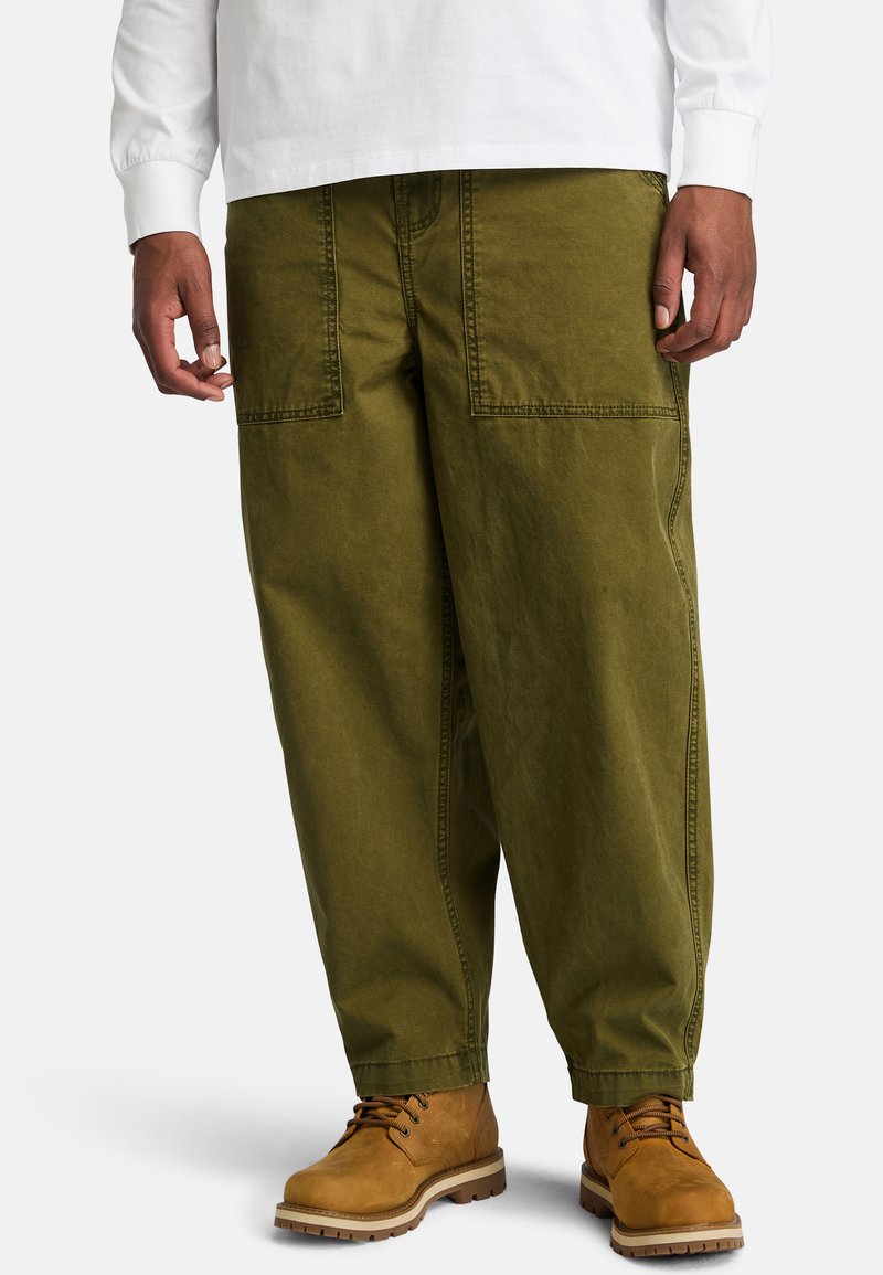 Olive green cotton cargo pants with two large front pockets and a relaxed fit, paired with brown lace-up boots.