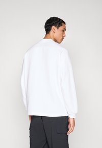 Λευκό μπλουζάκι μακρυμάνικο με ριμπ υφή, στρογγυλή λαιμόκοψη και άνετη εφαρμογή. Διαθέτει χαμηλωμένους ώμους και ίσια γραμμή στο τελείωμα.