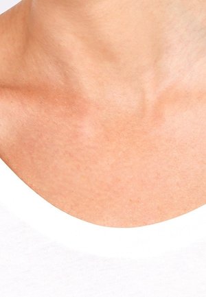 Gros plan sur le cou et le haut de la poitrine d'une personne portant une chemise blanche, montrant la texture naturelle de la peau et les détails de la clavicule.
