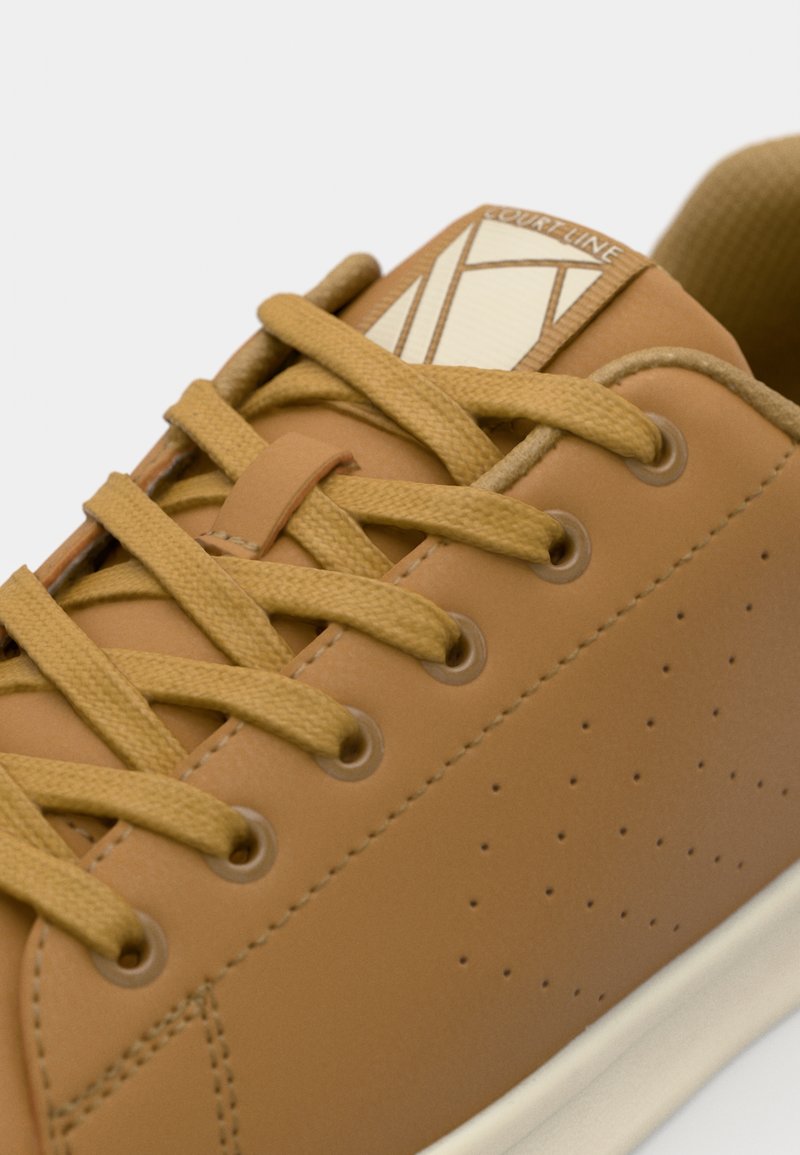 Zapatilla de cuero marrón con parte superior texturizada, punta redonda y diseño perforado. Presenta cordones beige y un logo cuadrado en la lengüeta.