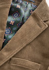 Blazer en velours côtelé marron avec une doublure intérieure à motif floral vert dans le revers et une poche passepoilée à l'avant.