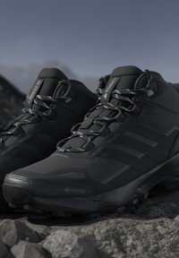 Sorte Adidas Terrex Gore-Tex vandresko med robuste såler og reflekterende snørebånd hvilende på klippefyldt udendørs terræn.