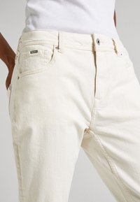 Ljust beige denim jeans med slim fit, med framfickor, bältesöglor och en metallknappstängning. Diskret logotag på midjebandet.