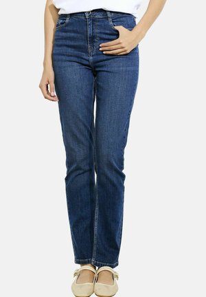 Jeans a vita alta blu scuro con una vestibilità slim. Presentano tasche anteriori, passanti per cintura e orli rifiniti. Indossati con ballerine chiare.