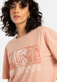 Lichtroze katoenen t-shirt met een grafisch ontwerp van abstracte vormen en palmbomen in een vervaagd oranje kleur. Losse pasvorm, korte mouwen.