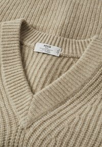 Pull côtelé beige en mélange laine et cachemire avec col en V et étiquette visible de la marque MNG Man cousue à l’intérieur.