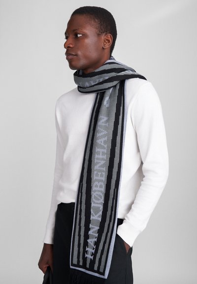 Kézzel kötött sál szürke és fekete csíkos mintával; a "HANKJØBENHAVN" szöveget tartalmazza; puha tapintású; végein fröcskölés részlet található.