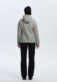 Light gray softshell jacket with a hood, displayed from the back. Paired with black pants and sturdy footwear. Minimalist design, no visible logos.