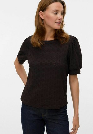 Zwarte textuur blouse met korte mouwen, een losse pasvorm en pofmouwen. Ronde halslijn en de zoom ligt boven de taille. Gedragen met donkere jeans.