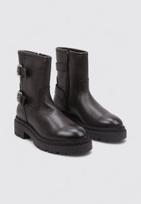 Botas de tobillo de cuero negro con acabado texturizado, cierre lateral con cremallera y dos detalles de hebilla metálica. Suela de goma gruesa que proporciona tracción.