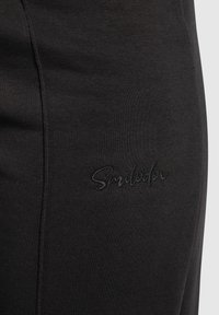 Svarta leggings gjorda av ett stretchigt tyg, med en diskret präglad logotyp. Materialet har en jämn och slät yta.